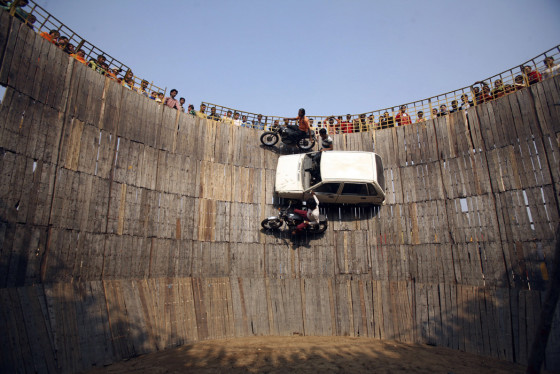 Stuntmen perform on their motorbikes and car on the walls of the \"Well of Death\" at a fair on the outskirts of Jammu